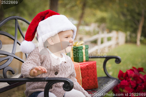 Image of Young Child Wearing Santa Hat Sitting with Christmas Gifts Outsi