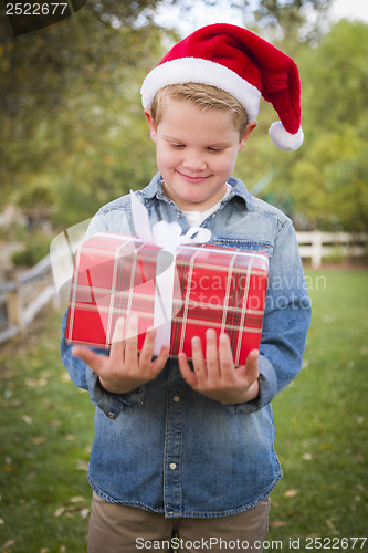 Image of Young Boy Wearing Santa Hat Holding Christmas Gift Outside