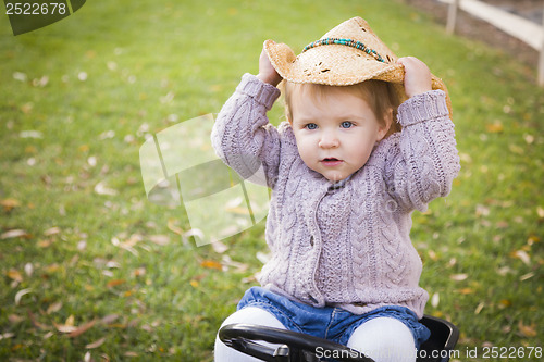 Image of Toddler Wearing Cowboy Hat and Playing on Toy Tractor Outside