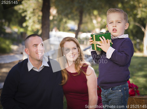 Image of Young Boy Holding Christmas Gift in Park While Parents Look