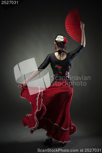 Image of young woman dancing flamenco with fan on black