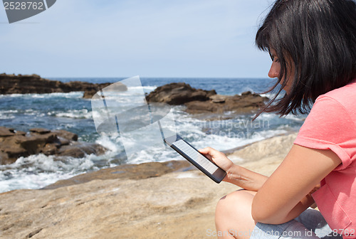 Image of Woman reading an e-book on beach