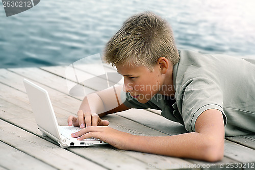 Image of Boy writing with computer at the sea