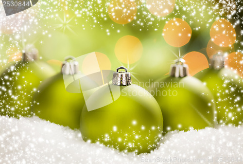 Image of Green Christmas Ornaments on Snow Over an Abstract Background