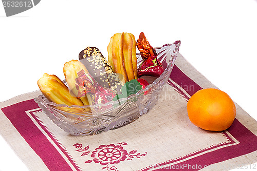 Image of Cakes and sweets in a crystal vase, a tangerine, a napkin on a w