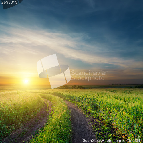 Image of sunset over dirty road in green fields