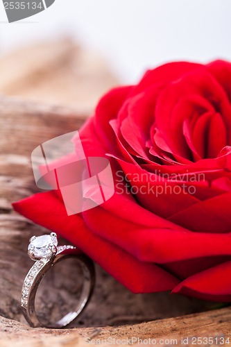 Image of beautiful ring on wooden background and red rose