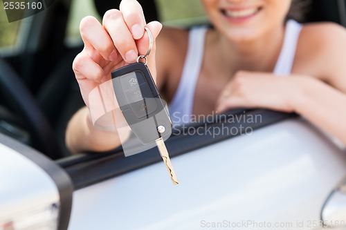 Image of young smiling woman sitting in car taking key 