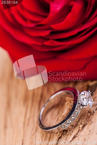 Image of beautiful ring on wooden background and red rose