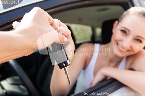 Image of young smiling woman sitting in car taking key 