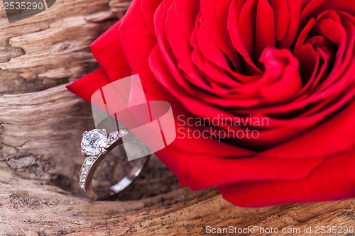 Image of beautiful ring on wooden background and red rose
