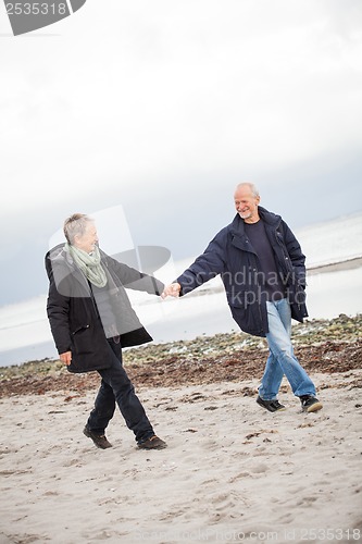 Image of mature happy couple walking on beach in autumn