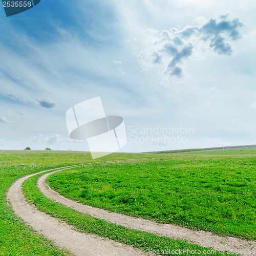 Image of dirty road in green grass under cloudy sky