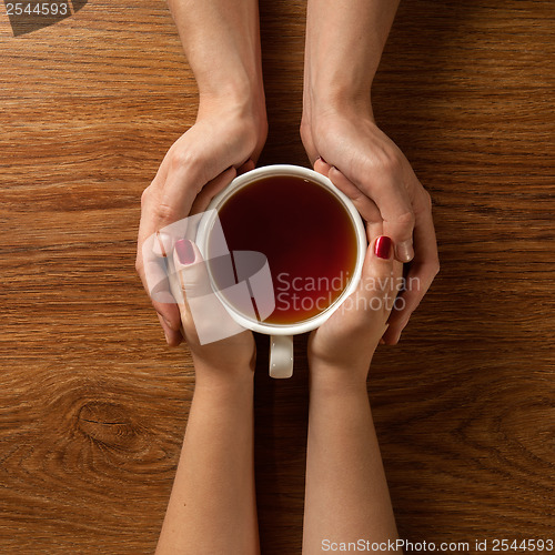 Image of woman holding hot cup of tea with cookies on wooden table