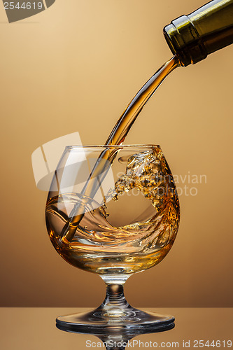 Image of Cognac pouring from bottle into glass with splash on brown backg