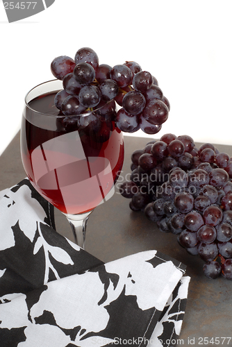 Image of Glass of red wine with grapes and a black and white napkin