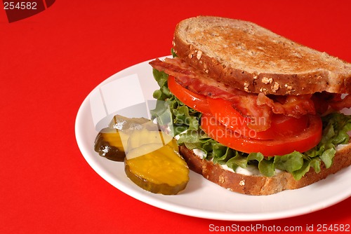 Image of Bacon, lettuce and tomato sandwich with pickles, red background