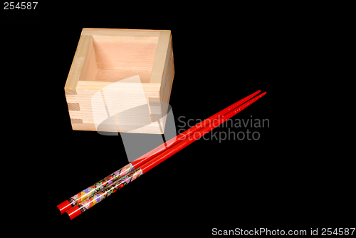 Image of Wooden sake cup with chopsticks on black background