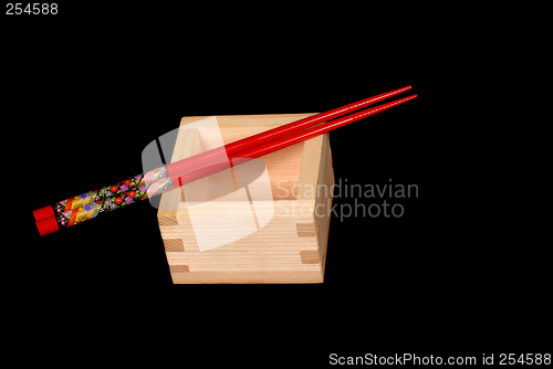 Image of Wooden sake cup with chopsticks resting on top on black backgrou