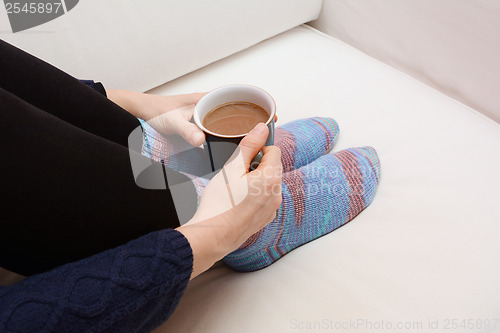 Image of Woman's hands holding a hot beverage, sitting on a couch