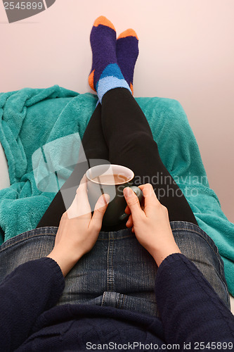 Image of Woman holding a hot drink, relaxing with her feet up