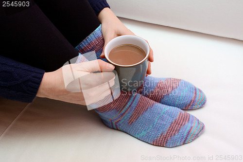 Image of Woman holding a hot drink, wearing warm knitted socks