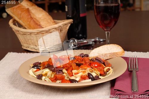 Image of A plate of pasta puttanesca with wine and bread