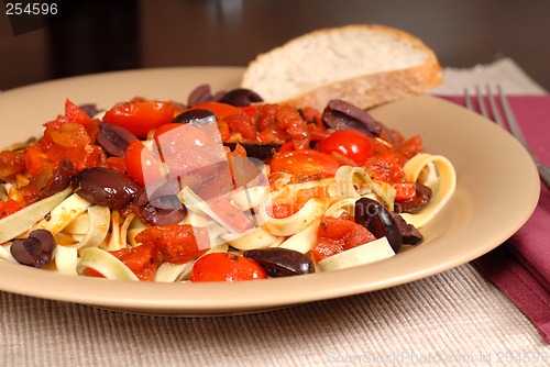 Image of Closeup of a plate of pasta puttanesca with wine and bread