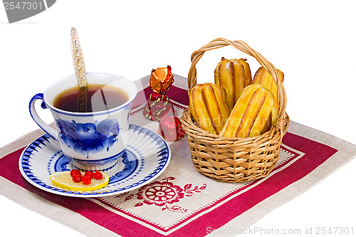 Image of Cup of tea , candies and cakes in a wicker basket.