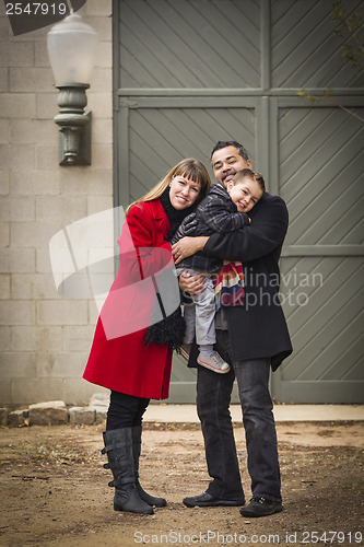 Image of Warmly Dressed Family Loving Son in Front of Rustic Building