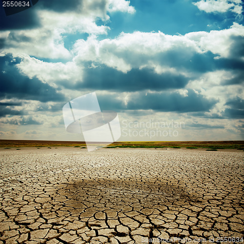 Image of wet spot on cracked earth under dramatic sky