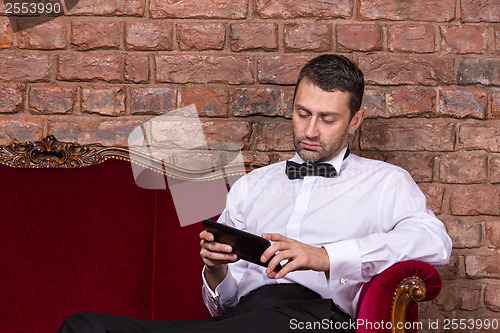 Image of Businessman lying on a settee and reading tablet