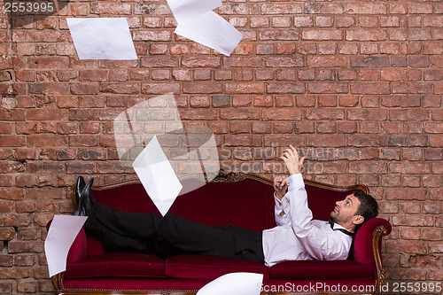 Image of Businessman lying on a settee with flying papers