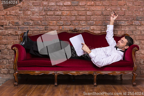 Image of Businessman lying on a settee and reading paperwork