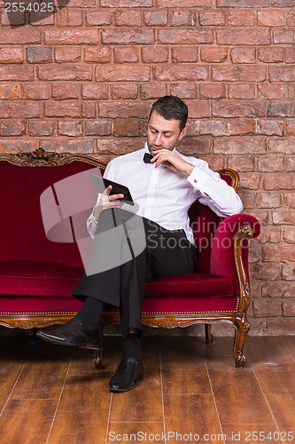 Image of Businessman lying on a settee and reading tablet