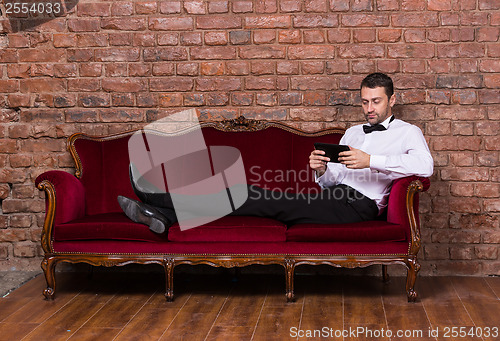 Image of Businessman lying on a settee and reading tablet