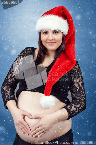 Image of beautiful pregnant santa woman tenderly holding her tummy