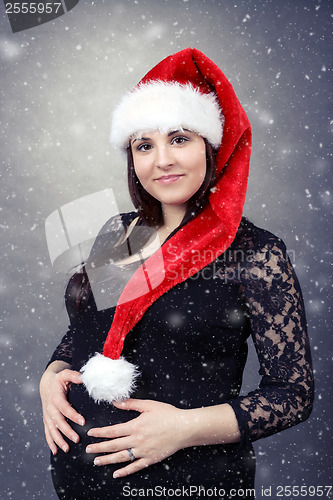 Image of beautiful pregnant santa woman tenderly holding her tummy