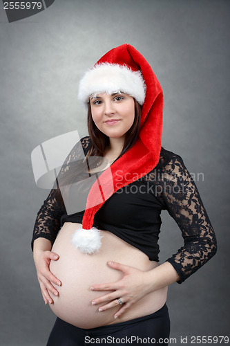 Image of beautiful pregnant santa woman tenderly holding her tummy