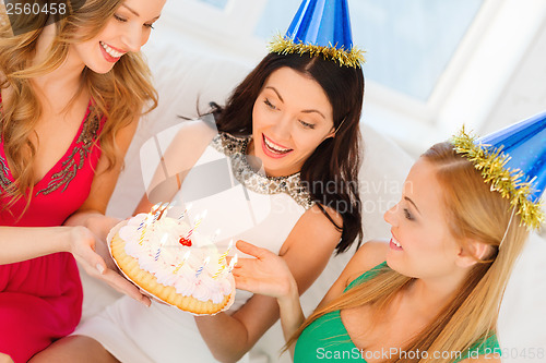 Image of three women wearing hats holding cake with candles