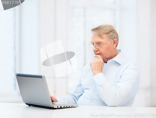 Image of old man in eyeglasses working with laptop at home