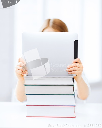 Image of girl hiding behind tablet pc and books at school