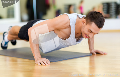 Image of smiling man doing push-ups in the gym