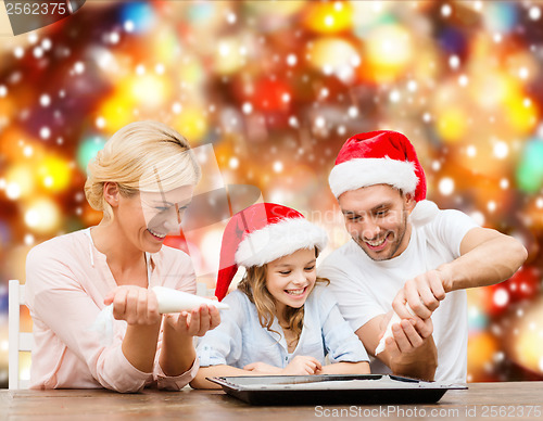 Image of happy family in santa helper hats making cookies