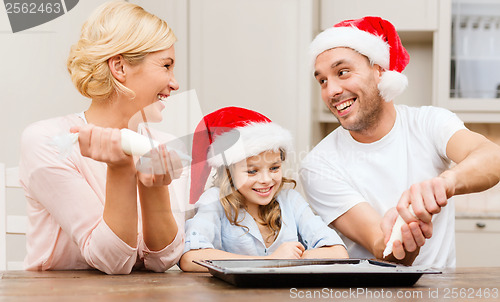 Image of happy family in santa helper hats making cookies