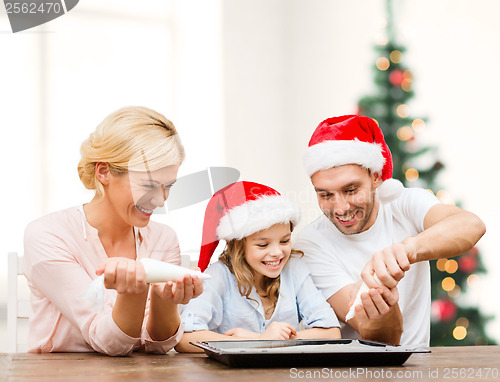 Image of happy family in santa helper hats making cookies