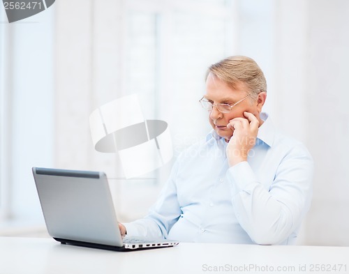 Image of old man in eyeglasses working with laptop at home