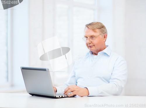 Image of old man in eyeglasses working with laptop at home