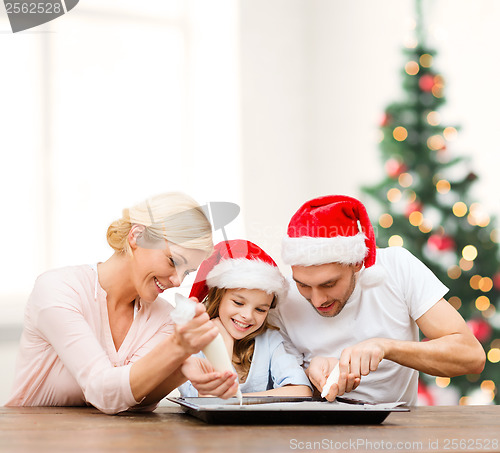 Image of happy family in santa helper hats making cookies