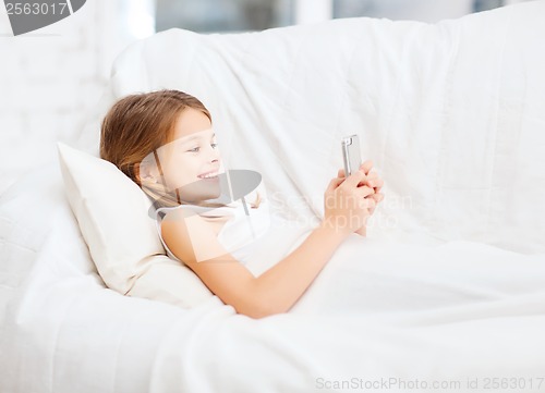 Image of little girl with smartphone playing in bed